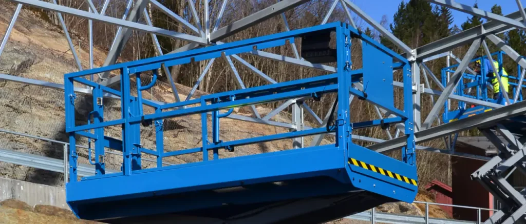 Egy kék ollós emelő platformja magasban, egy acélszerkezetű építkezésen, szemléltetve az emelőgépkezelő tanfolyam gyakorlati hasznát.